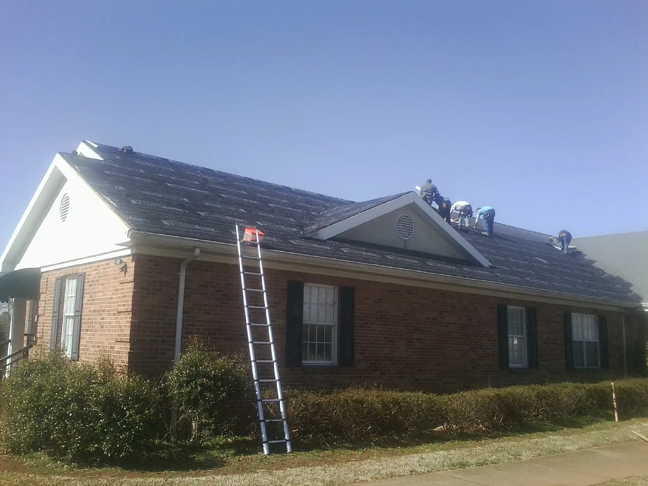 Crew tearing shingles off a brick ranch roof with a ladder set — Emergency Roof Repair work by our crew in Paragon