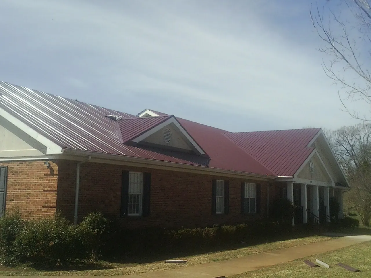 Red metal roof with gabled entries on a long brick building, from a Hail Damage Roof Repair job in Paragon