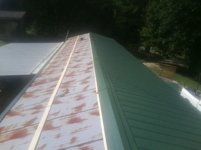 Old rusted panels beside newly installed green metal roofing — Wind Damage Roof Repair by Roofing Brothers in Paragon