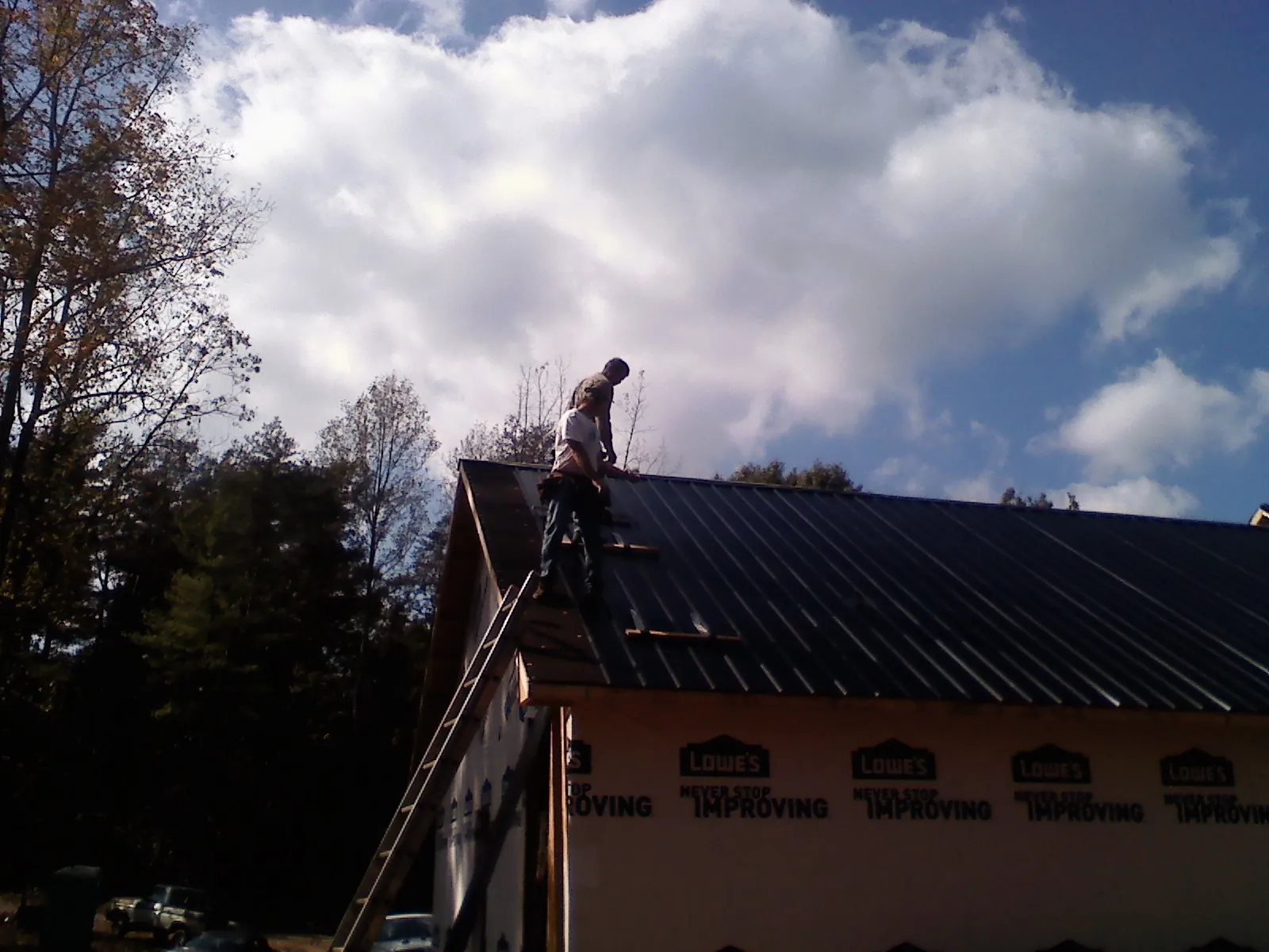 Roofer fastening dark metal panels high against a cloudy sky, from a Roof Inspection job in Paragon