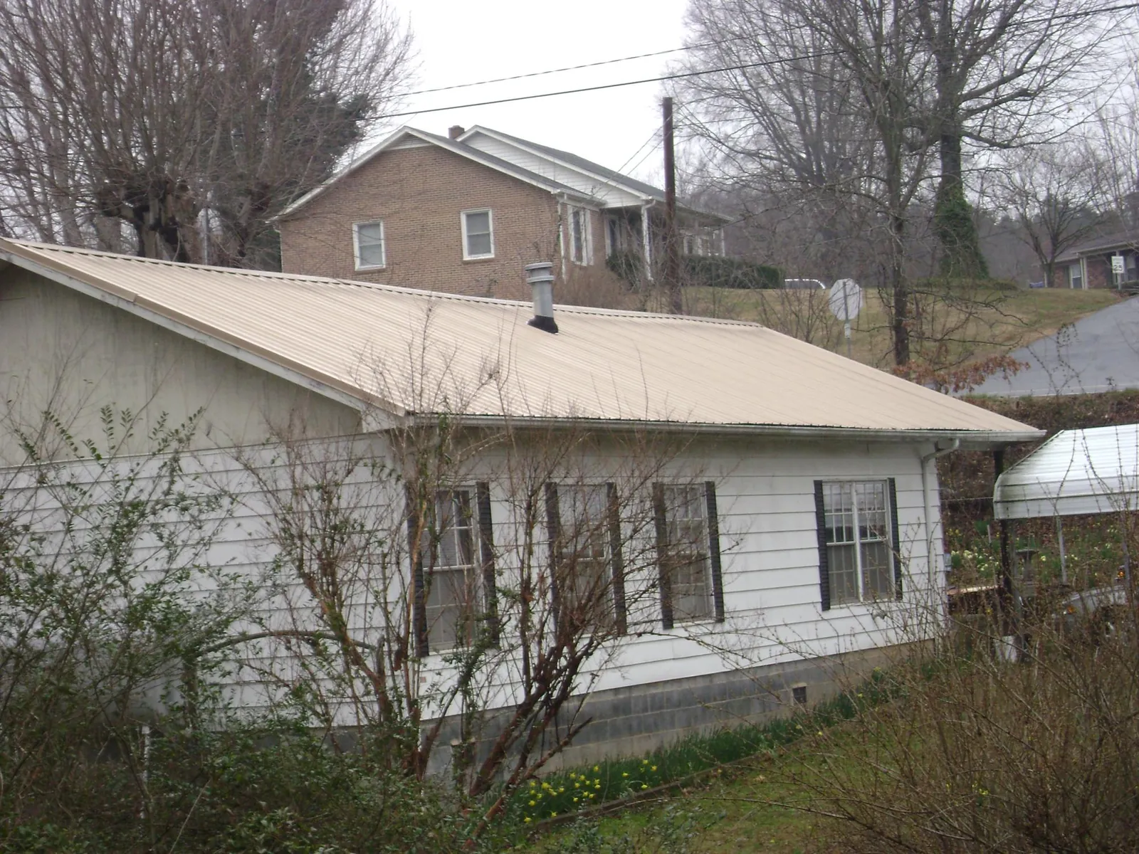 Tan metal roof on a white sided house set into a hillside — Commercial Roofing by Roofing Brothers in Paragon