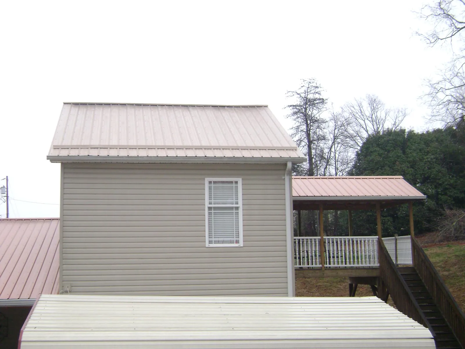 Tan metal roofs on a two story addition and attached porch, from a Roof Replacement job in Paragon